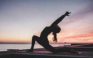 Frau macht Yoga am Meer im Sonnenuntergang